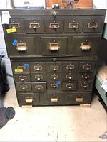 Front view of green vintage metal library cabinet with 25 drawers, showing worn condition and label tags on drawers.
