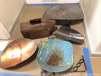 Group of 5 metal items on floor showing two scoops, two holders, one bucket in various states of rust and wear.