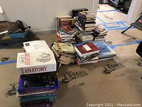 Wide view of stacks of various hardcover and softcover books placed on the floor, covering topics including medical, history, and military.