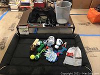 Photo showing the dog bed with various dog toys, dog mugs, a knitted dog vest, nail clippers, and the small garbage pail scattered on the bed