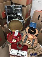 Photo showing galvanized steel box with costume jewelry inside, red and green round velvet jewelry boxes containing assorted pins, rings, and necklaces with visible wear