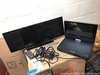 Panasonic SC-HC37 long CD player and Sony DVP-FX810 portable DVD player together with cables and remote control on cardboard box.