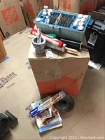 Top level view of marble mortar and pestle, rolling pins on cardboard box, baking cookbooks and copper baking mold on floor