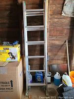Full view of aluminum extension ladder leaning against wood wall among garage items