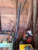 Full view of black metal lally column support beam leaning against wood wall with other items around.