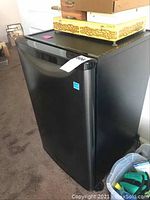 Front angle view of the black Darby mini fridge showing smooth door and sticker.