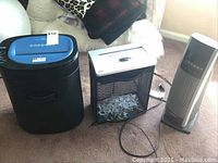Photo showing both paper shredders and tower heater on carpet with couch background.