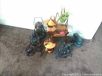 Wide photo of metal decor items grouped on carpet including Buddhas, dragons, lantern, ant sculpture, and small wooden stool