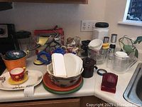 Overview of assorted kitchen ceramics and glassware including teapots, bowls, jars, funnels, and measuring cups on kitchen counter.