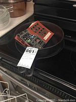 Two Wagner cast iron pans stacked on an oven stove top with a red and black vintage East Iron Cookbook on top.