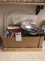 Box containing assorted baking accessories including cookie cutters of multiple shapes, baking tins, and decorative tools in a plastic container.