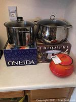 Image of the Oneida and Triomphe stainless steel pots with glass lids and the Descoware red enamel cast iron pot displayed together on a countertop.