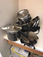 Photo showing stacked stainless steel pots with lids and a pressure cooker on countertop.