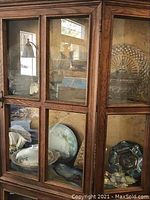 Photo of two shelves inside a wooden glass cabinet showing a blue china plate, clear decorative glass plates and bowls, and other items.