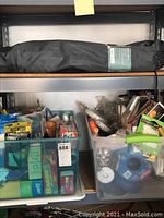 Two plastic bins on a shelf filled with assorted household items like Kleenex, cleaning sponges, tape, and tools.