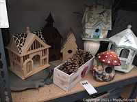 Shelf display of multiple decorative birdhouses and mushroom house, wooden planter with pinecones