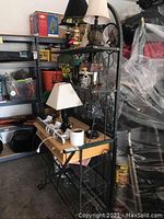 Full view of the bakers rack showing wood shelves and metal frame with various lamps on it.