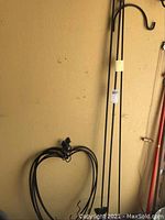 Four smaller black metal garden decor pieces with decorative tops and hooks for hanging items, against a wall, labeled with lot tag.