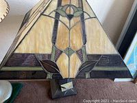 Close-up of stained glass lamp shade with geometric beige, brown and green glass pieces and a metal base.