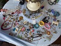 Wide view of assorted costume jewelry on a table, showing variety of necklaces, bracelets, pins, earrings.