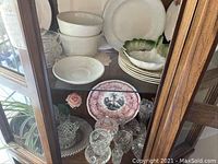 Two shelves of crystal glassware, ironstone bowls, decorative plates including vintage transferware plate and green ceramic leaf bowl