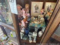 View showing 2 shelves in a wood cabinet with various ceramic collectibles including figurines and a miniature tea set