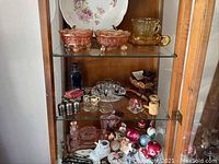 Photo of three wooden shelves inside a cabinet displaying collectibles arranged densely including glassware, pipes and small decorative items