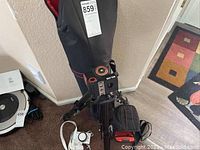 Photo of the black tripod standing on the floor with its padded carrying case behind it.