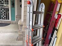Folded ladder leaning against exterior wall showing aluminum rails with orange plastic components