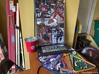 Colorado Avalanche hockey poster collage on table with red bucket and sports pennants leaning against wall, also a black folder with Avalanche logo