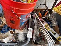 Photo of bucket top view showing caulking tubes and applicator tool with adjacent bin filled with various tools and hardware.