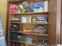 Photo of shelves showing Brillo soap pads, cleaning brushes, safety goggles, and assorted small cleaning supplies and hardware items in plastic containers and bags.