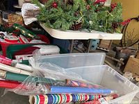 Side view of folding table with artificial greenery and rolls of wrapping paper underneath. Contents not included.