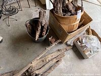 Weathered logs and wood pieces laid on floor beside metal bucket holding more wood pieces.