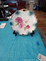 Full front view of antique ceramic plate on a stand with floral rose center and ornate rim