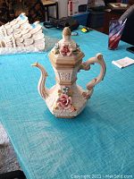 Full view of the hexagonal ceramic pitcher vase with ornate handle, lid, and applied flowers.