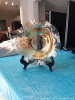 Large iridescent amber carnival glass fruit bowl with wavy edges on black stand facing camera, set on blue tablecloth