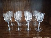 Front view showing all 8 crystal wine glasses arranged on a wooden surface, showcasing their ornate etched floral patterns.