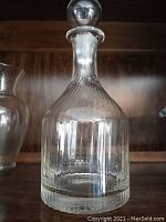 Vintage clear cut glass decanter with swirled vertical lines and a round stopper on a wood shelf
