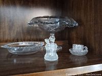Photo showing the candy dish, miniature coffee cup with saucer, sugar jar, and small spoons on a wooden shelf.