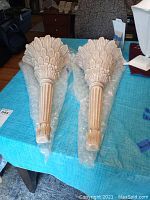 Pair of large white wall sconces with intricate carved designs wrapped on bubble wrap on a blue cloth.