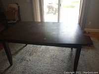 Front view of dark wood rectangular dining table with visible surface wear and an extension leaf removed and resting to the side.