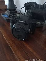 Panasonic Lumix DCM-FZ20 camera with attached lens and lens cover along with black drawstring lens pouch shown on a wooden surface.