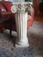 White ceramic pedestal with classical ionic column design, showing fluted shaft and intricate volute scrolls with floral touch.