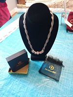 Necklace on black necklace stand with box and pouch on table