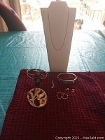 Lot display on red cloth with brooch, bracelets, pendant, necklace chain, and earrings arranged around a white jewelry display bust.