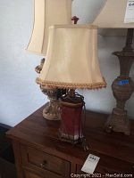Red and gold decorative vintage lamp with gold fabric lampshade on wooden table, shown from front.