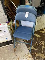 Front view of one blue folding chair showing padded seat and back, metal frame, chair folded behind.