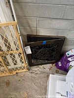 View of two metal scrollwork panels. One panel leans against a wall near a wooden baby gate.