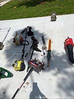 Photo showing STIHL leaf blower, Ryobi weed eater, various attachments, CB 720 blower laid out on concrete.
